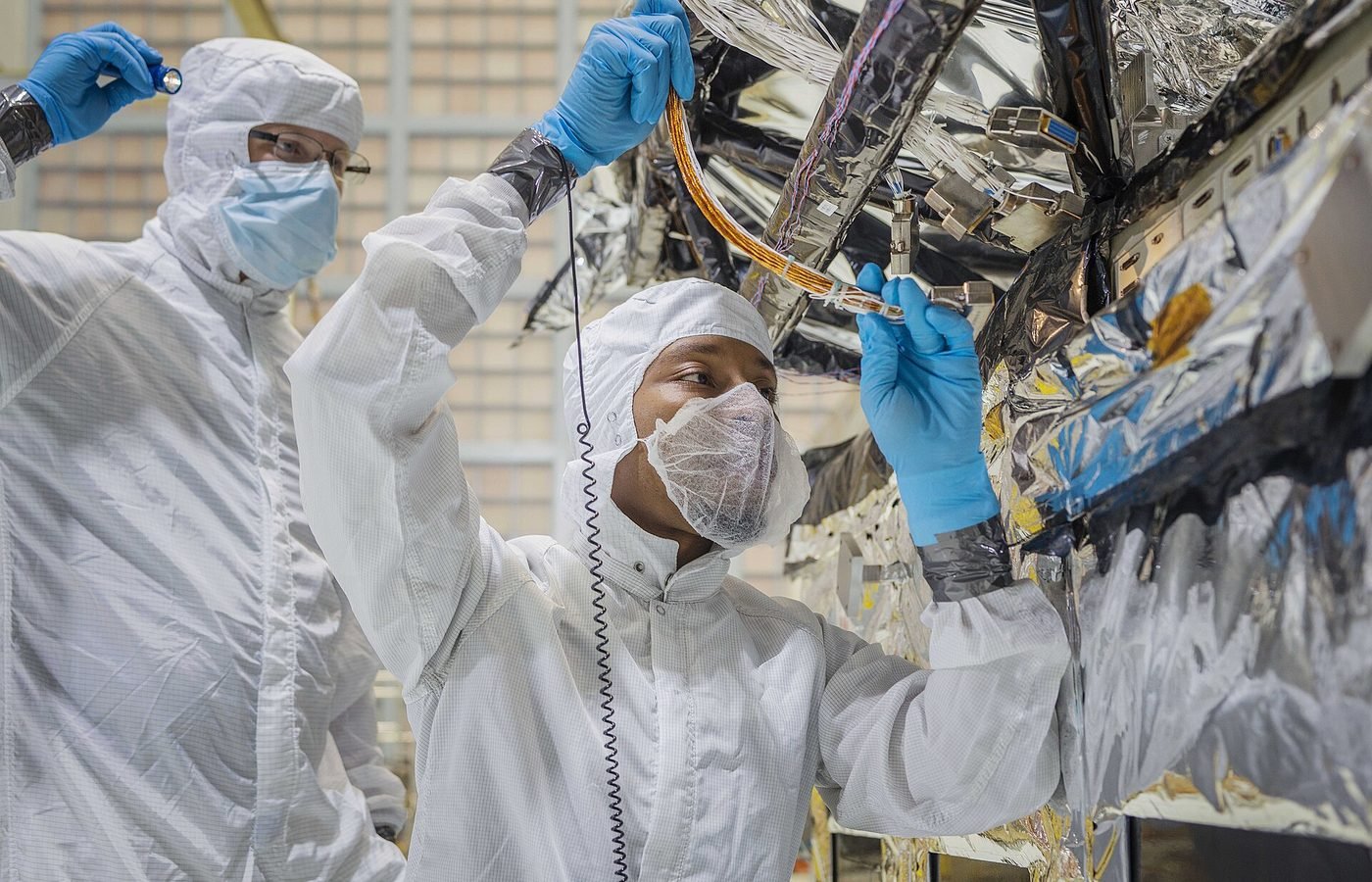 Due tecnici in camera bianca collegano un cablaggio su un satellite rivestito di isolante multistrato